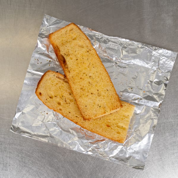 Two slices of golden-brown garlic bread with herbs, resting on crumpled aluminum foil.