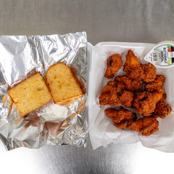 Fried chicken wings with buttermilk ranch dressing and two slices of Texas toast on a metal surface.