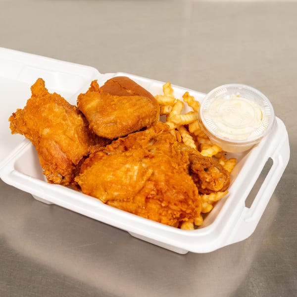 Fried chicken pieces, crinkle-cut fries, a dinner roll, and coleslaw in a white takeout container.