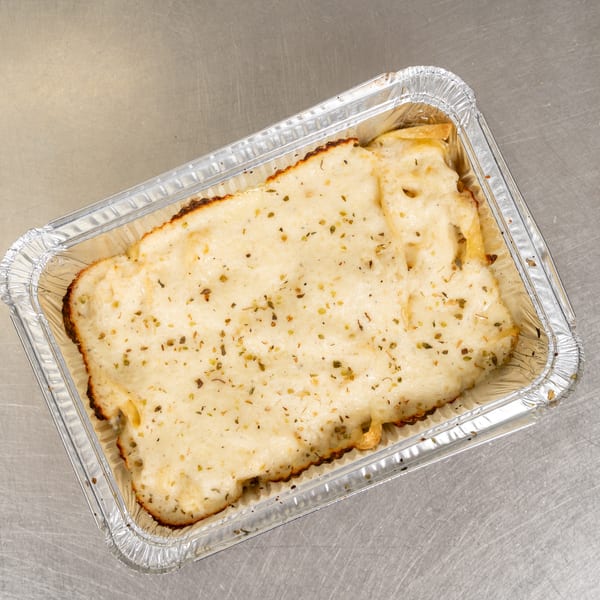 Baked lasagna with melted cheese and herbs in a foil container on a metal surface.