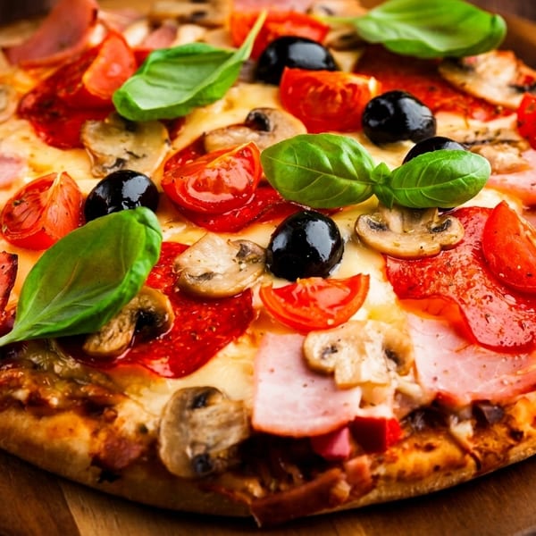 A delicious pizza with ham, mushrooms, tomatoes, olives, and basil on a wooden board.