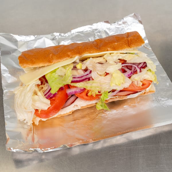 A large sub sandwich with cheese, lettuce, red onion, and tomatoes on foil.