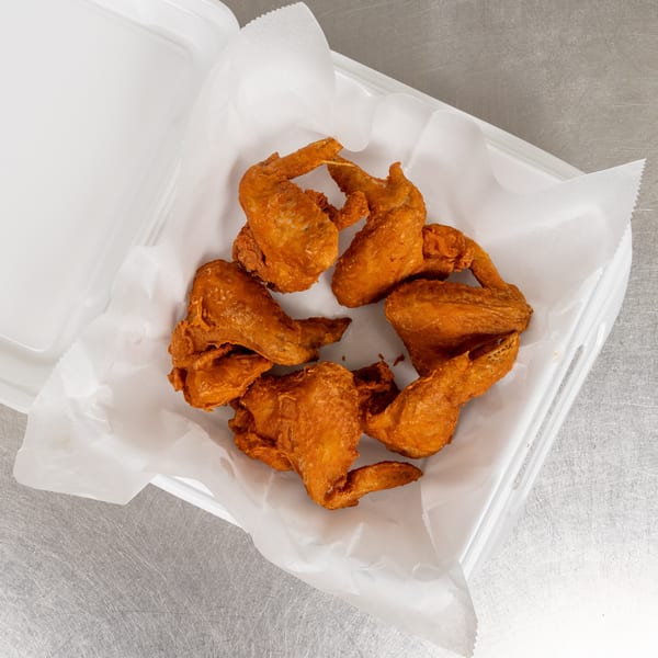 Crispy fried chicken wings in a white takeout container lined with parchment paper.