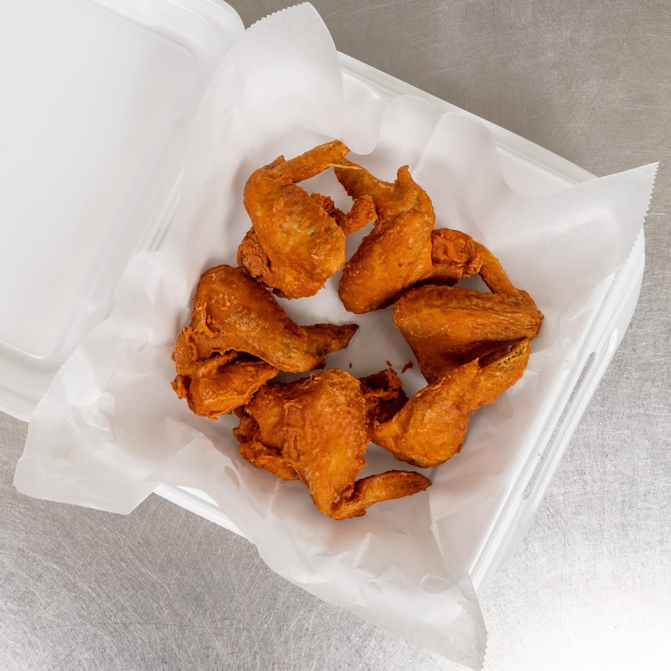 Crispy fried chicken wings in a white takeout container lined with parchment paper.