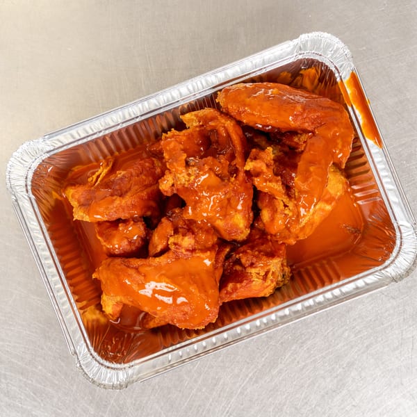 Buffalo chicken wings in a foil takeout container, drenched in bright orange sauce.