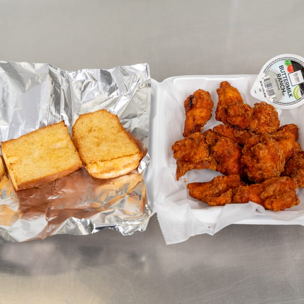 Fried chicken wings with a side of garlic bread and ranch dressing in takeout containers.