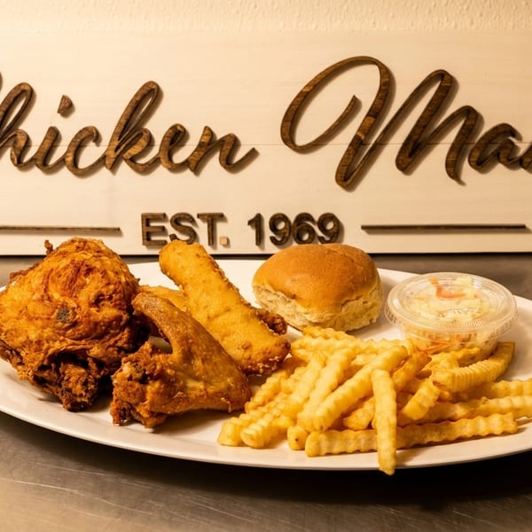 A fried chicken meal with fries, a roll, and coleslaw on a white plate in front of a "Chicken Man" sign.